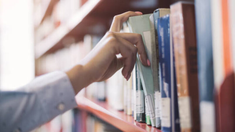 Photograph of someone's arm searching through books on a library shelf