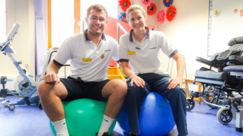 Two physiotherapists sat on therapy balls in a rehab space