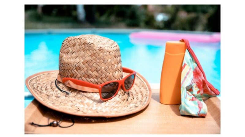 sun hat, sunglasses and sun tan lotion next to a swimming pool.